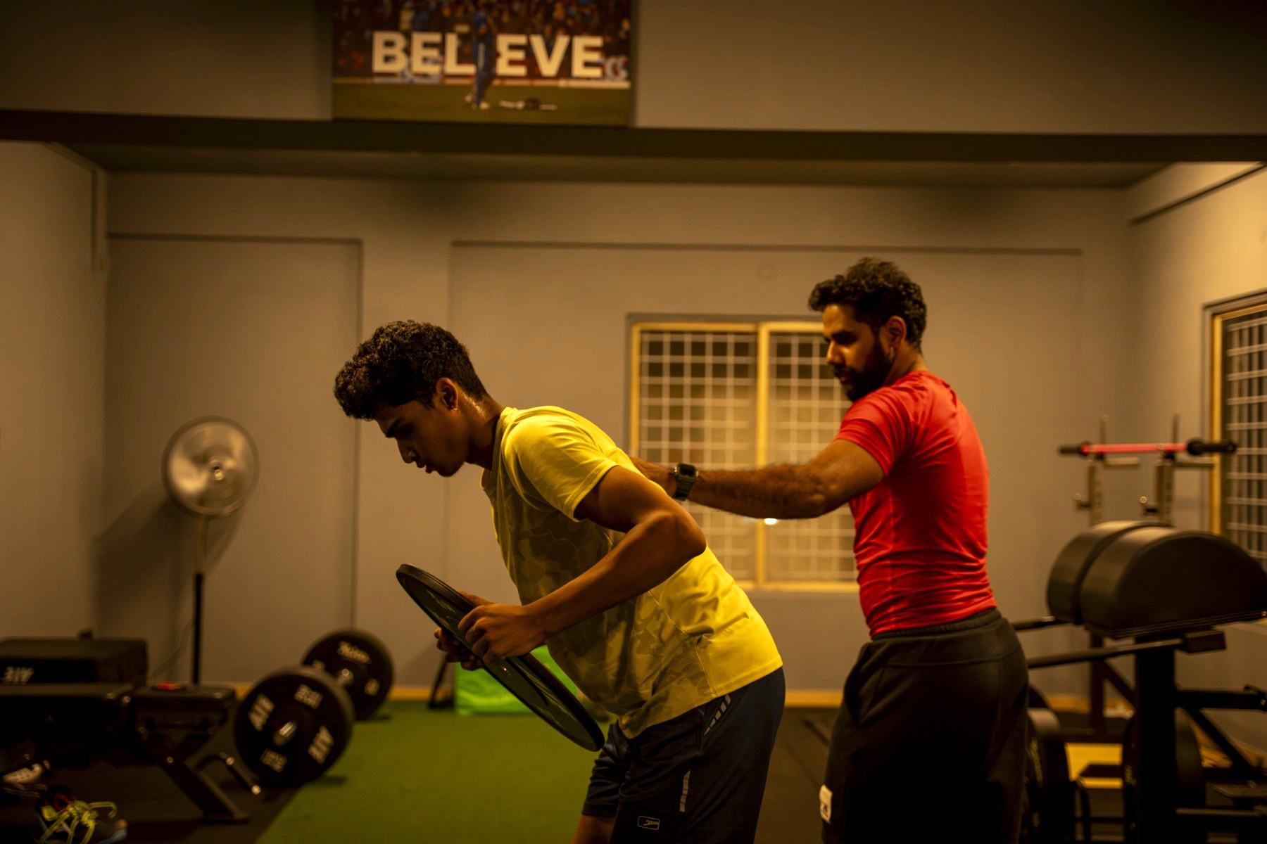 Strength coach correcting an athlete's form during a sports rehab session at UnReal Performance, Kasturi Nagar, Bengaluru